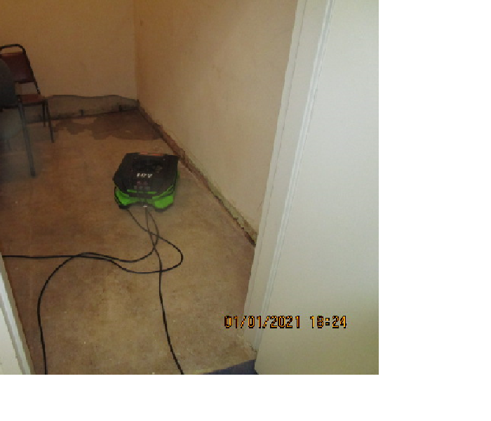 Air mover blowing a puddle of water coming from the corner of a below grade room with concrete walls.