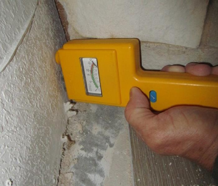 Moisture testing meter with pins stuck into drywall showing a very wet reading