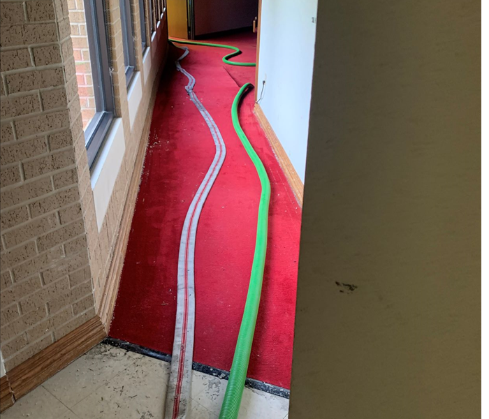 Fire department hose and SERVPRO of Waco hose laying side by side in hallway of a fire damaged building