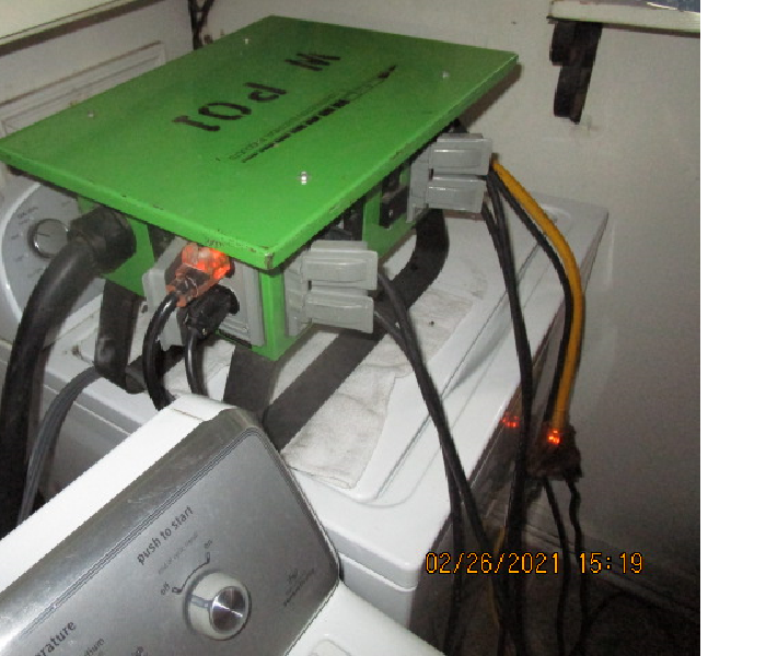 Green power box with many cords plugged into it sitting upon a dryer